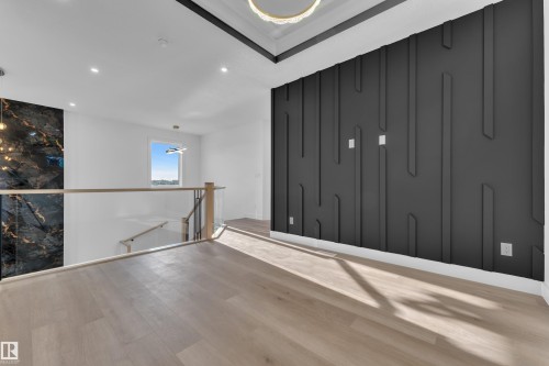 Wood-finish flooring, custom accent wall, recessed lighting, glass panel railing, and a black marble-style accent wall - 2039 156 Avenue Nw, Edmonton, AB - Indoor Photo Showing Other Room