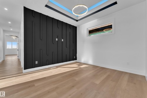 Wood-finish flooring throughout, tray ceiling with accent lighting, contemporary ceiling fixture, accent wall paneling, and a horizontal window - 2039 156 Avenue Nw, Edmonton, AB - Indoor Photo Showing Other Room