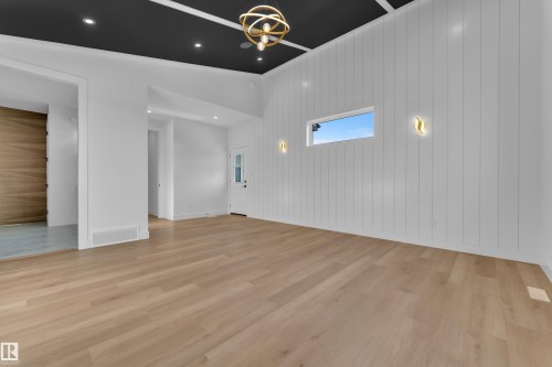 Light wood-finish flooring, white vertical plank wall paneling, a rectangular horizontal window, and a dark ceiling with recessed lighting and a decorative light fixture - 2039 156 Avenue Nw, Edmonton, AB - Indoor Photo Showing Other Room