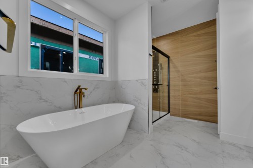Freestanding soaking tub with a floor-mounted gold-tone faucet, walk-in shower with wood-finish tile surround, and white marble-look floor and wall tile - 2039 156 Avenue Nw, Edmonton, AB - Indoor Photo Showing Bathroom