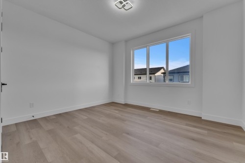 Spacious room featuring wood-finish flooring, a large window, a ceiling-mounted light fixture, and white wall finishes - 2039 156 Avenue Nw, Edmonton, AB - Indoor Photo Showing Other Room