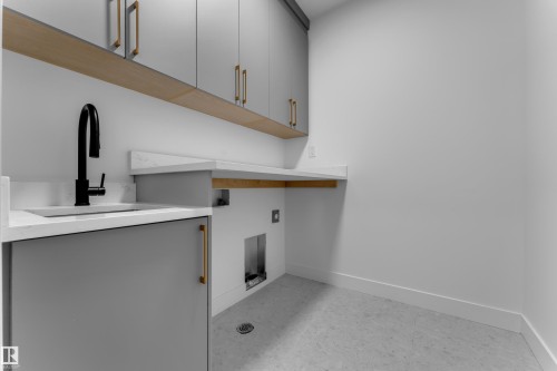 Matte black gooseneck faucet, light grey cabinetry with gold-tone hardware, integrated sink, light countertop surfaces, and an overhead lighting fixture - 2039 156 Avenue Nw, Edmonton, AB - Indoor Photo Showing Other Room