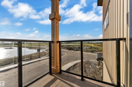 Balcony featuring glass panel railing, wood-finish decking, and an exposed structural wood column - 2039 156 Avenue Nw, Edmonton, AB - Outdoor With Balcony With View