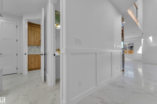 Bright hallway showcasing crisp white walls with classic wainscoting, polished stone-finish flooring, and multiple wood-finish doors with brass hardware - 2039 156 Avenue Nw, Edmonton, AB - Indoor Photo Showing Other Room