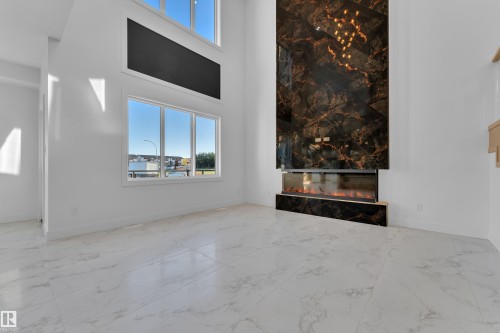 Two-story living area featuring a full-height stone-look accent wall, an integrated linear fireplace, and large windows - 2039 156 Avenue Nw, Edmonton, AB - Indoor Photo Showing Other Room