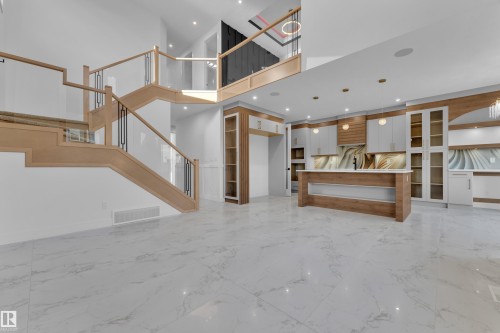 Open-concept living area with large-format tile flooring, a custom staircase featuring glass and wood railings, and a modern kitchen with a central island and integrated appliances - 2039 156 Avenue Nw, Edmonton, AB - Indoor Photo Showing Other Room
