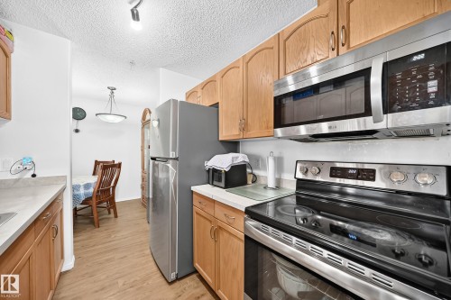 Wood-finish flooring, recessed lighting, wood cabinetry, stainless steel appliances, and solid surface countertops - #324 279 Suder Greens Dr Nw, Edmonton, AB - Indoor Photo Showing Kitchen