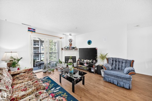 Bright living room with hardwood flooring, multiple seating areas, and built-in entertainment cabinetry - #324 279 Suder Greens Dr Nw, Edmonton, AB - Indoor Photo Showing Living Room With Fireplace