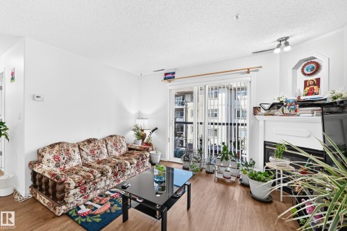 Wood-finish flooring, white walls, built-in fireplace, recessed alcove, and a sliding glass door to a balcony - #324 279 Suder Greens Dr Nw, Edmonton, AB - Indoor Photo Showing Living Room