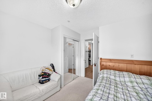 Mirrored closet doors, flush-mount ceiling light, white wall paint, and light-colored carpet flooring - #324 279 Suder Greens Dr Nw, Edmonton, AB - Indoor Photo Showing Bedroom