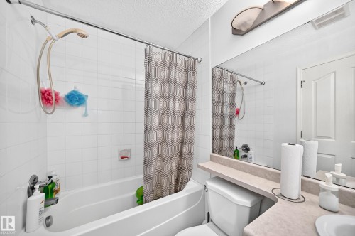 White tile surround bathtub with shower fixture - #324 279 Suder Greens Dr Nw, Edmonton, AB - Indoor Photo Showing Bathroom
