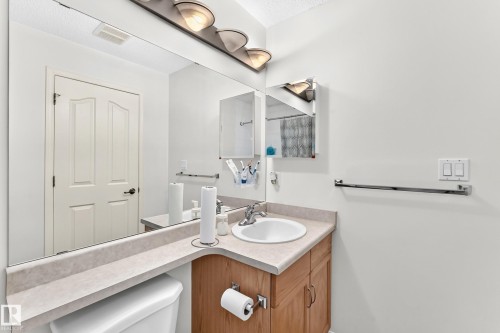 Bathroom featuring an integrated sink, wood-finish cabinetry, a large vanity mirror, and a wall-mounted light fixture - #324 279 Suder Greens Dr Nw, Edmonton, AB - Indoor Photo Showing Bathroom