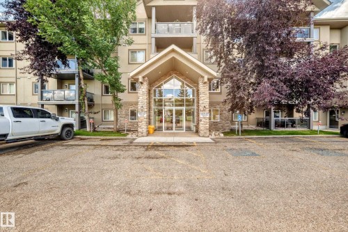Stone-accented building entrance with prominent glazing, individual balconies with glass railings, and a paved parking area - #324 279 Suder Greens Dr Nw, Edmonton, AB - Outdoor With Balcony With Facade