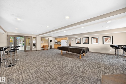 Spacious recreation room featuring recessed lighting, patterned carpeting, a functional kitchenette with wood-finish cabinetry, and double glass-paneled doors - #324 279 Suder Greens Dr Nw, Edmonton, AB - Indoor Photo Showing Other Room