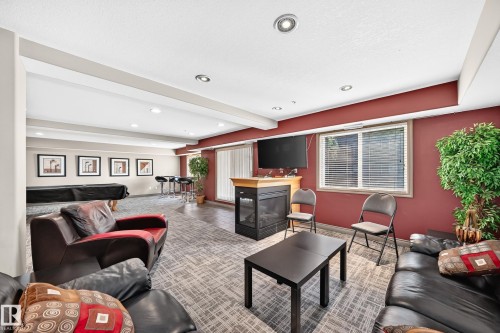 Recessed lighting throughout, accent wall, built-in fireplace, wall-mounted television, and wood-finish flooring - #324 279 Suder Greens Dr Nw, Edmonton, AB - Indoor Photo Showing Living Room