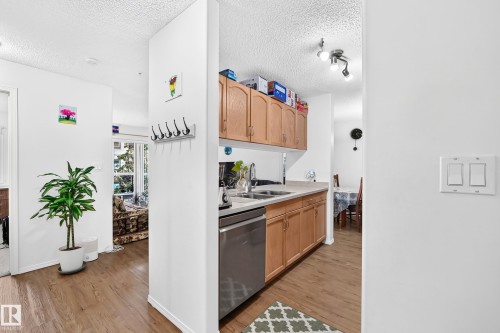 Wood-finish flooring throughout, with light wood cabinetry, light-colored countertops, and a stainless steel dishwasher - #324 279 Suder Greens Dr Nw, Edmonton, AB - Indoor Photo Showing Kitchen With Double Sink