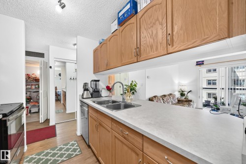 Kitchen featuring wood-finish cabinetry, stainless steel double basin sink, and ample counter space - #324 279 Suder Greens Dr Nw, Edmonton, AB - Indoor Photo Showing Kitchen With Double Sink