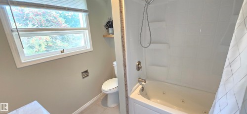 Bathroom featuring a white bathtub with jets, a shower-head with flexible hose, and a white toilet - 4317 50 Street, Vegreville, AB - Indoor Photo Showing Bathroom