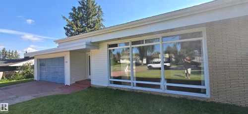 White horizontal siding exterior with a brick accent wall, large picture windows, and an attached garage with a blue door - 4317 50 Street, Vegreville, AB - Outdoor