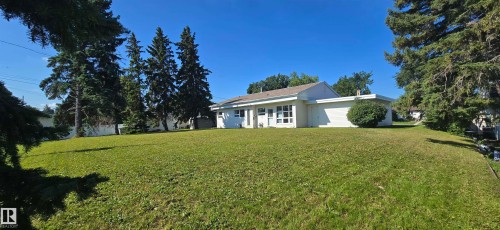 Expansive green lawn with mature evergreen trees and a white-sided residence featuring multiple windows - 4317 50 Street, Vegreville, AB - Outdoor