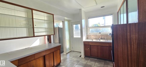 Kitchen featuring wood-finish cabinetry, solid surface countertops, a mosaic tile backsplash, and tile flooring - 4317 50 Street, Vegreville, AB - Indoor Photo Showing Other Room