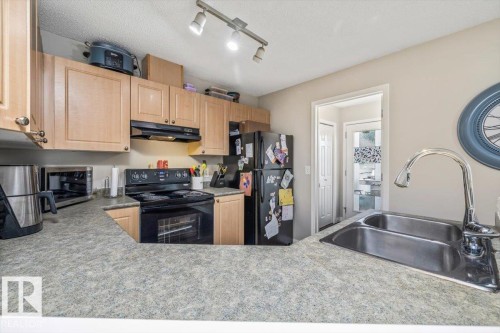 Kitchen featuring light wood-finish cabinetry, a double basin stainless steel sink, and a black electric range - 4744 Terwillegar Common Nw, Edmonton, AB - Indoor Photo Showing Kitchen With Double Sink
