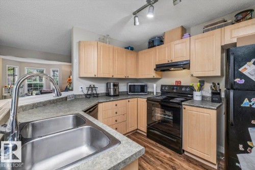Full kitchen featuring wood-finish cabinetry, a double basin stainless steel sink, black appliances, and track lighting - 4744 Terwillegar Common Nw, Edmonton, AB - Indoor Photo Showing Kitchen With Double Sink