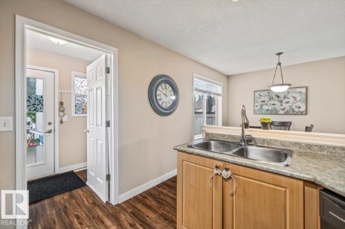 Kitchen featuring wood-finish flooring, a double basin stainless steel sink, and light wood cabinetry with a laminate countertop - 4744 Terwillegar Common Nw, Edmonton, AB - Indoor Photo Showing Kitchen With Double Sink