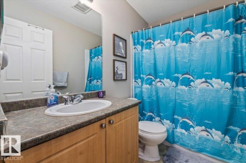 Bathroom featuring a single vanity with an integrated sink, a dark countertop, wood-finish cabinetry, and a toilet - 4744 Terwillegar Common Nw, Edmonton, AB - Indoor Photo Showing Bathroom