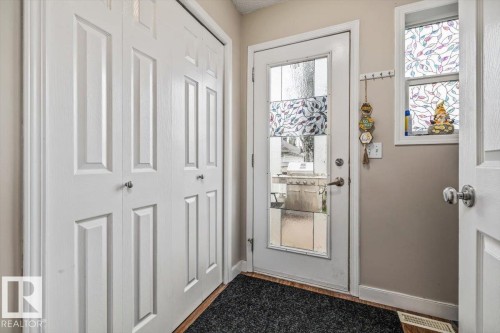 White paneled bi-fold closet doors, full-light exterior door with decorative glass, and wood-finish flooring - 4744 Terwillegar Common Nw, Edmonton, AB - Indoor Photo Showing Other Room