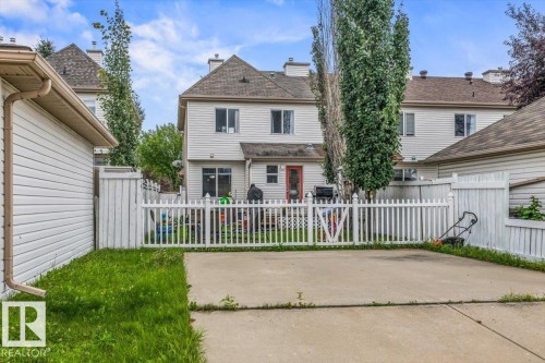 Rear exterior with light-colored siding, a white picket fence, and a concrete patio - 4744 Terwillegar Common Nw, Edmonton, AB - Outdoor