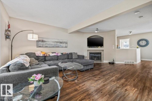 Wood-finish flooring, recessed lighting, built-in fireplace, and a kitchen pass-through window create a cohesive living space - 4744 Terwillegar Common Nw, Edmonton, AB - Indoor Photo Showing Living Room With Fireplace