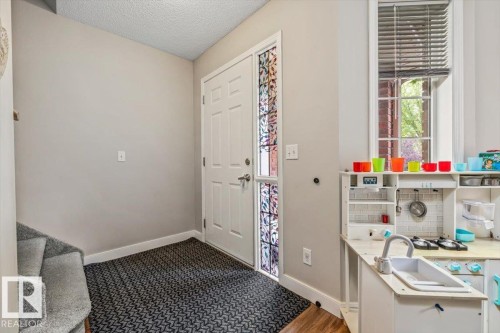 Entryway featuring a paneled door with decorative glass sidelight, patterned floor covering, and a carpeted staircase - 4744 Terwillegar Common Nw, Edmonton, AB - Indoor