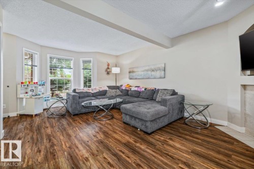 Wood-finish flooring throughout, featuring a bay window with multiple panes, recessed ceiling lighting, and light-toned wall finishes - 4744 Terwillegar Common Nw, Edmonton, AB - Indoor Photo Showing Living Room With Fireplace