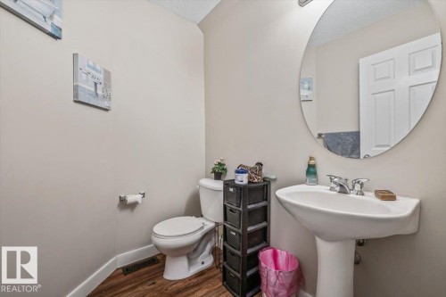 Pedestal sink with chrome fixtures, oval wall mirror, and wood-finish flooring - 4744 Terwillegar Common Nw, Edmonton, AB - Indoor Photo Showing Bathroom