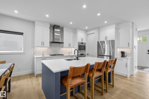Kitchen featuring white cabinetry, a large center island with a white countertop and integrated sink, stainless steel appliances, and a tile backsplash - 7314 Morgan Road Nw, Edmonton, AB - Indoor Photo Showing Kitchen With Upgraded Kitchen