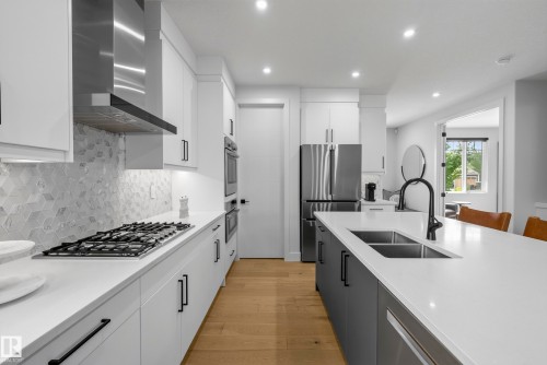 White cabinetry with dark hardware, stainless steel appliances, wood-finish flooring, white countertops, and a dual-basin sink with a matte black faucet - 7314 Morgan Road Nw, Edmonton, AB - Indoor Photo Showing Kitchen With Double Sink With Upgraded Kitchen