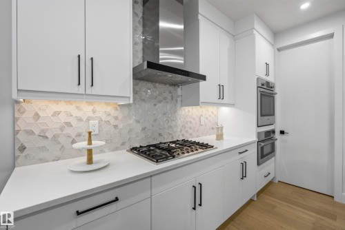 White cabinetry with matte black hardware, integrated gas cooktop, stainless steel range hood, built-in double ovens, and patterned backsplash - 7314 Morgan Road Nw, Edmonton, AB - Indoor Photo Showing Kitchen With Upgraded Kitchen