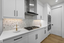 White cabinetry with matte black hardware, integrated gas cooktop, stainless steel range hood, built-in double ovens, and patterned backsplash - 