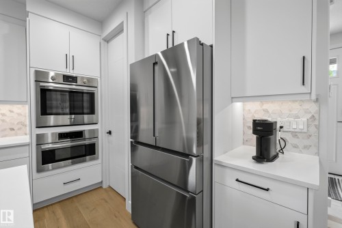 Stainless steel built-in double ovens, stainless steel French door refrigerator, white shaker-style cabinetry with black pulls, light wood-finish flooring, and a patterned tile backsplash - 7314 Morgan Road Nw, Edmonton, AB - Indoor Photo Showing Kitchen