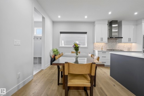 Modern kitchen featuring light-toned wood-finish flooring, white cabinetry, a stainless steel range hood, and a dark-toned island with a light countertop - 7314 Morgan Road Nw, Edmonton, AB - Indoor