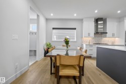Modern kitchen featuring light-toned wood-finish flooring, white cabinetry, a stainless steel range hood, and a dark-toned island with a light countertop - 