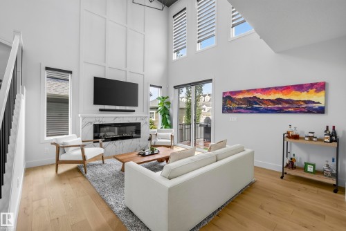 Vaulted ceilings, wood-finish flooring, a contemporary fireplace with a marble-finish surround, and a sliding glass door to a balcony - 7314 Morgan Road Nw, Edmonton, AB - Indoor Photo Showing Living Room With Fireplace