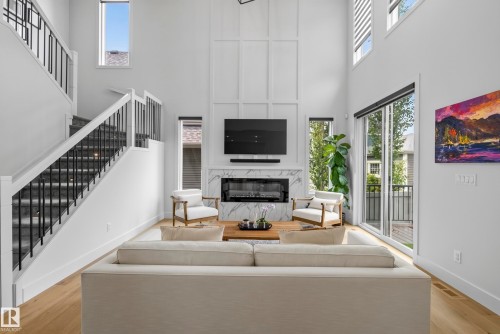 Two-story living area with a fireplace, a double-height wall featuring panel molding, and wood-finish flooring - 7314 Morgan Road Nw, Edmonton, AB - Indoor With Fireplace