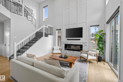 Two-story living area featuring wood-finish flooring, a contemporary fireplace with a stone surround, and a two-story staircase with a wrought iron railing - 7314 Morgan Road Nw, Edmonton, AB - Indoor Photo Showing Living Room With Fireplace