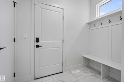 White painted doors with matte black hardware, built-in bench with storage, integrated wall hooks, and large format tile flooring - 