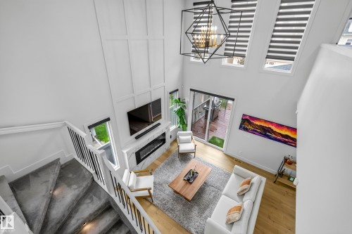 High ceilings, wood-finish flooring, staircase with dark metal balusters, fireplace with stone surround, and abundant natural light - 7314 Morgan Road Nw, Edmonton, AB - Indoor Photo Showing Other Room
