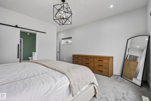 Geometric chandelier, barn door entry, recessed lighting, white walls, and gray carpeting - 7314 Morgan Road Nw, Edmonton, AB - Indoor Photo Showing Bedroom