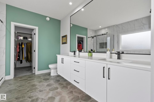 Spacious bathroom featuring a dual sink vanity, white countertops, hexagon-patterned floor tiles, a large wall-mounted mirror, and a walk-in shower with a sliding glass door - 7314 Morgan Road Nw, Edmonton, AB - Indoor Photo Showing Bathroom
