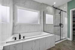 Soaking tub with matte black fixtures, an adjacent glass-enclosed shower with a black frame, white tiled walls with subtle veining, and hexagonal floor tiling - 
